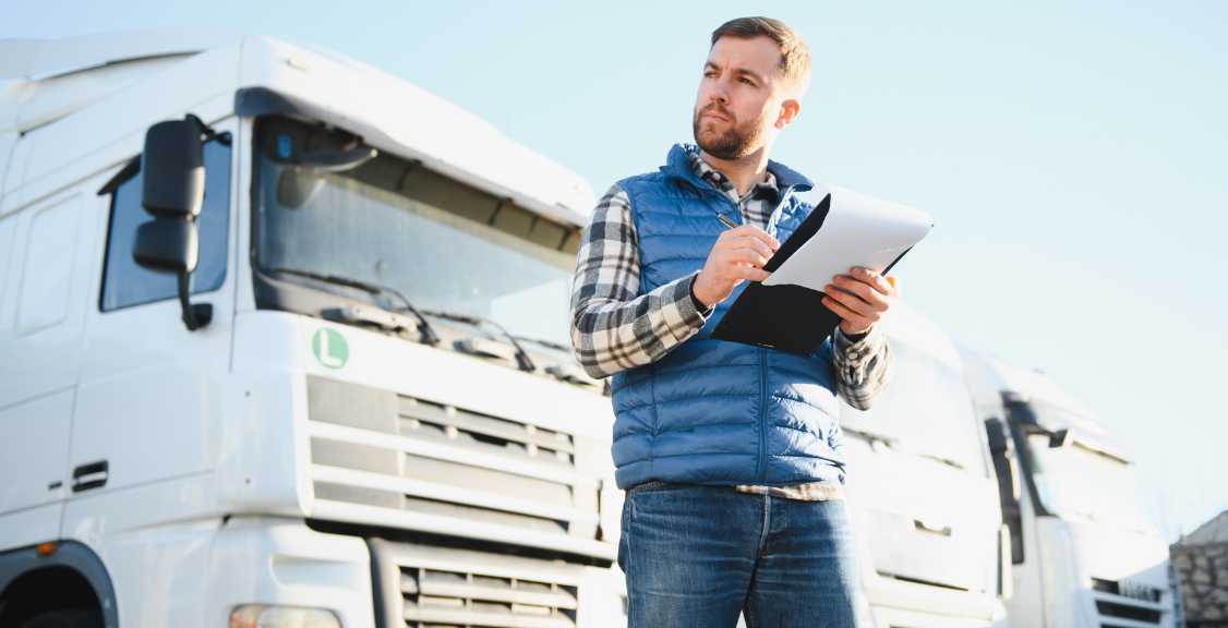 A handsome truck driver stands on the background of a truck in the parking lot
