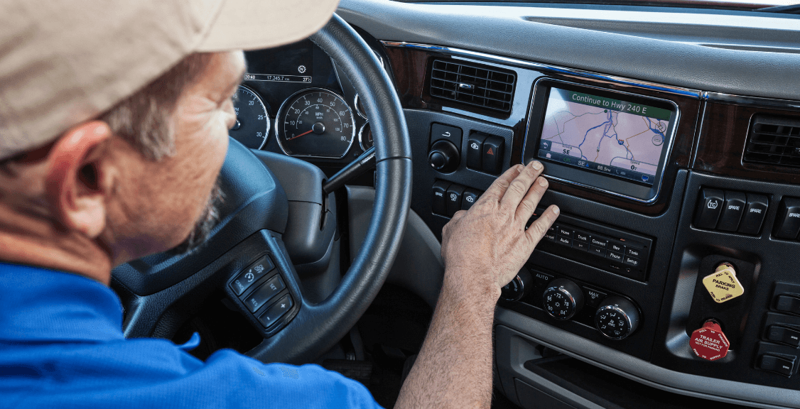 A truck driver is seen adjusting or viewing the GPS navigation system in the truck's dashboard, which is used for real-time tracking and route planning.