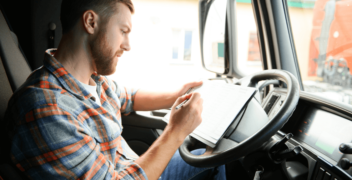 driver sits behind the wheel of a truck and examines documentation