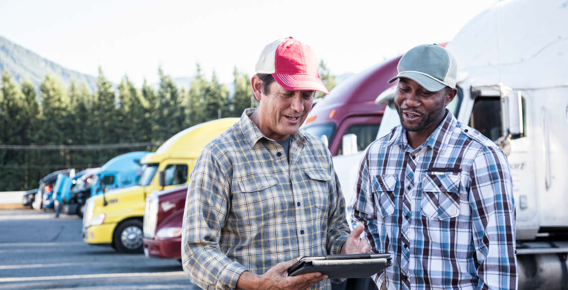  man and a black man truck driving team together in a truck stop parking lot